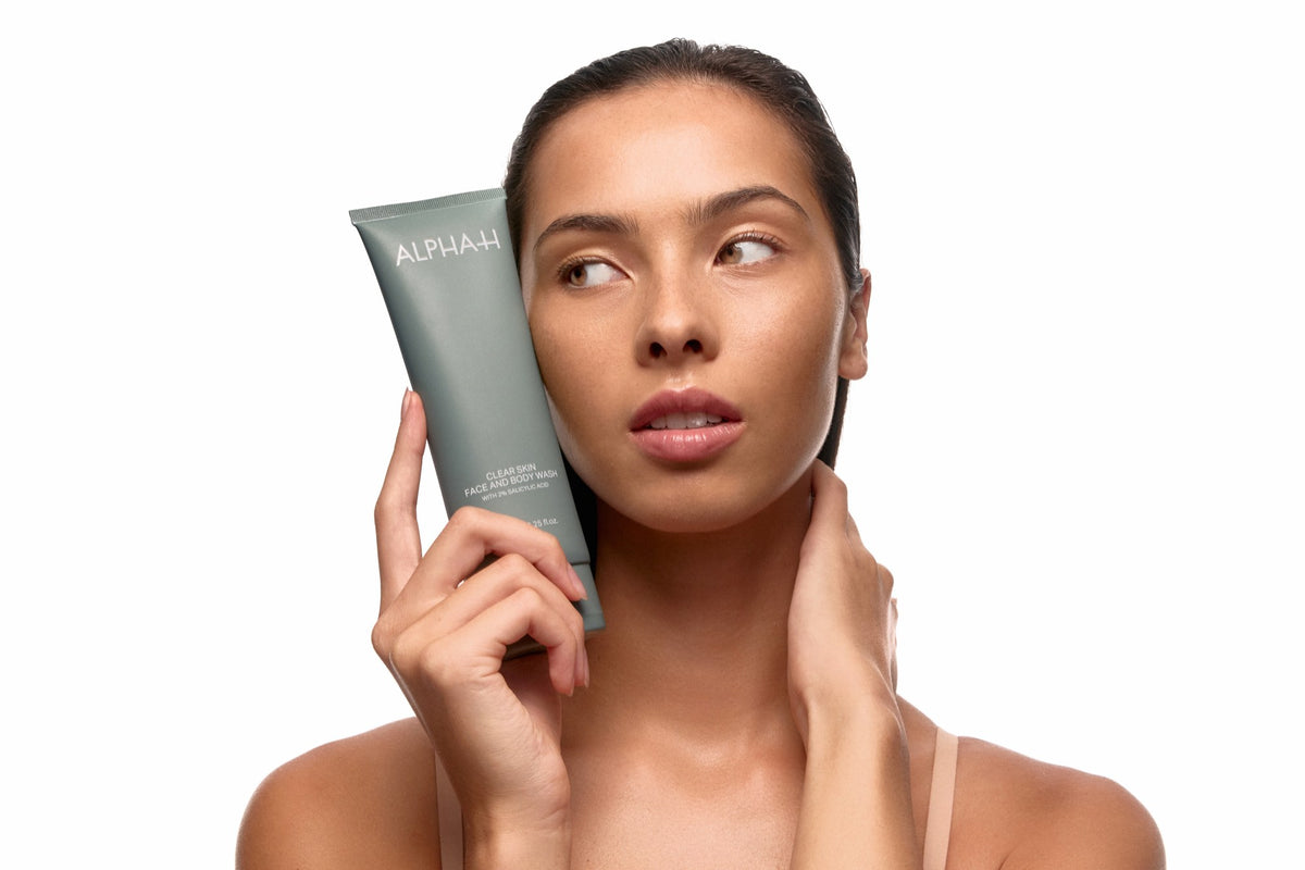 Alpha-H Clear Skin Face & Body Wash modella con il tubo accanto al viso