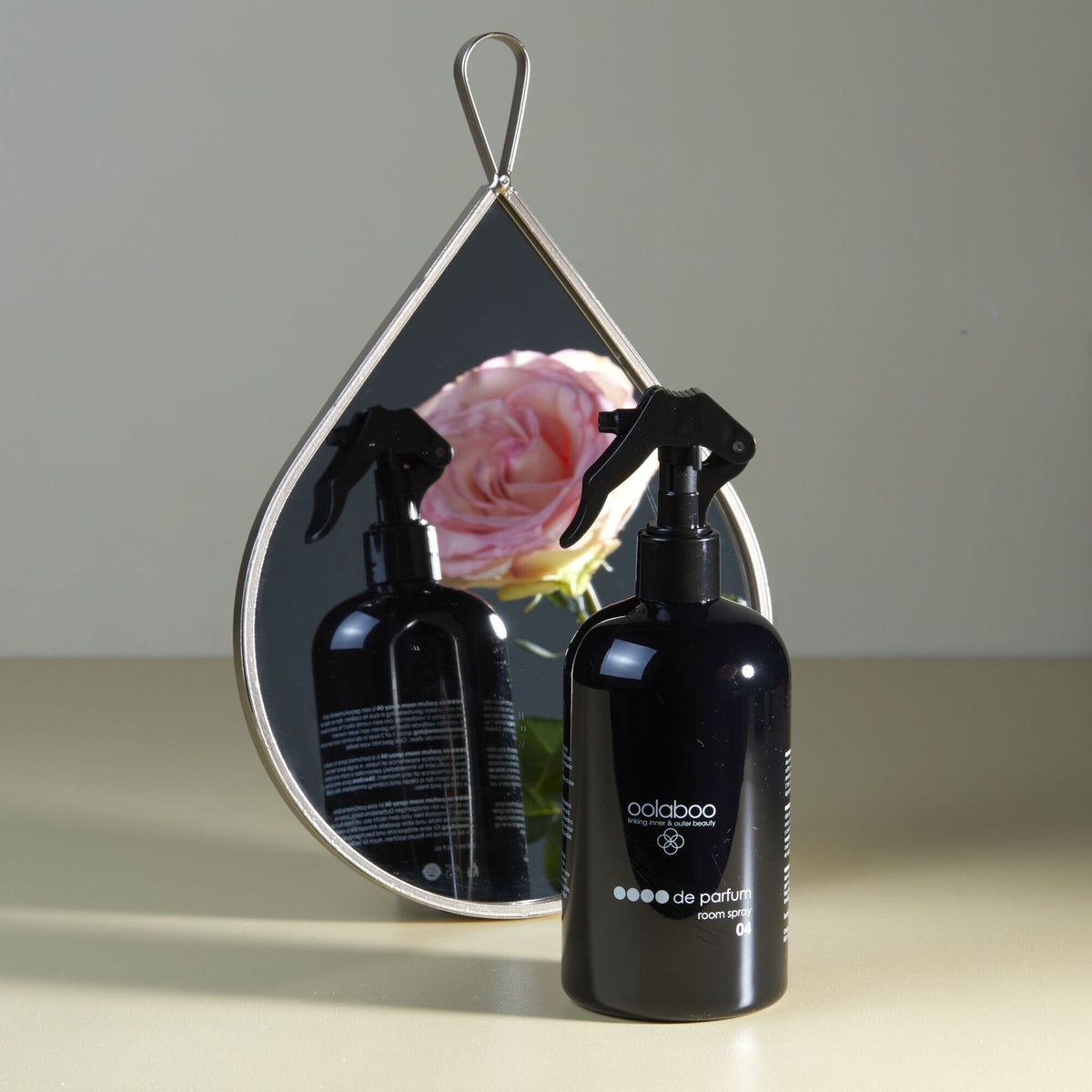 Oolaboo OOOO de Parfum Room Spray davanti a uno specchio con rosa